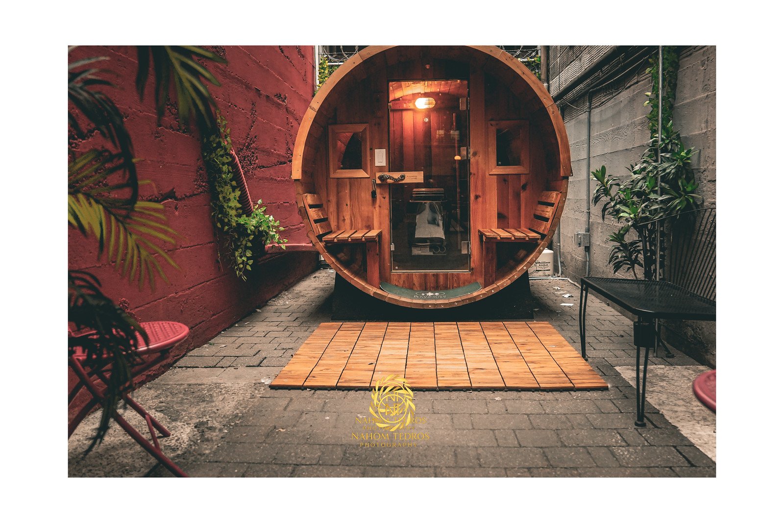 Round wooden barrel sauna in a plant-lined courtyard