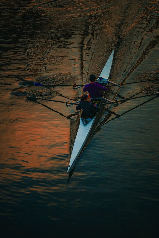 Two rowers in a racing shell on sunset water, seen from above